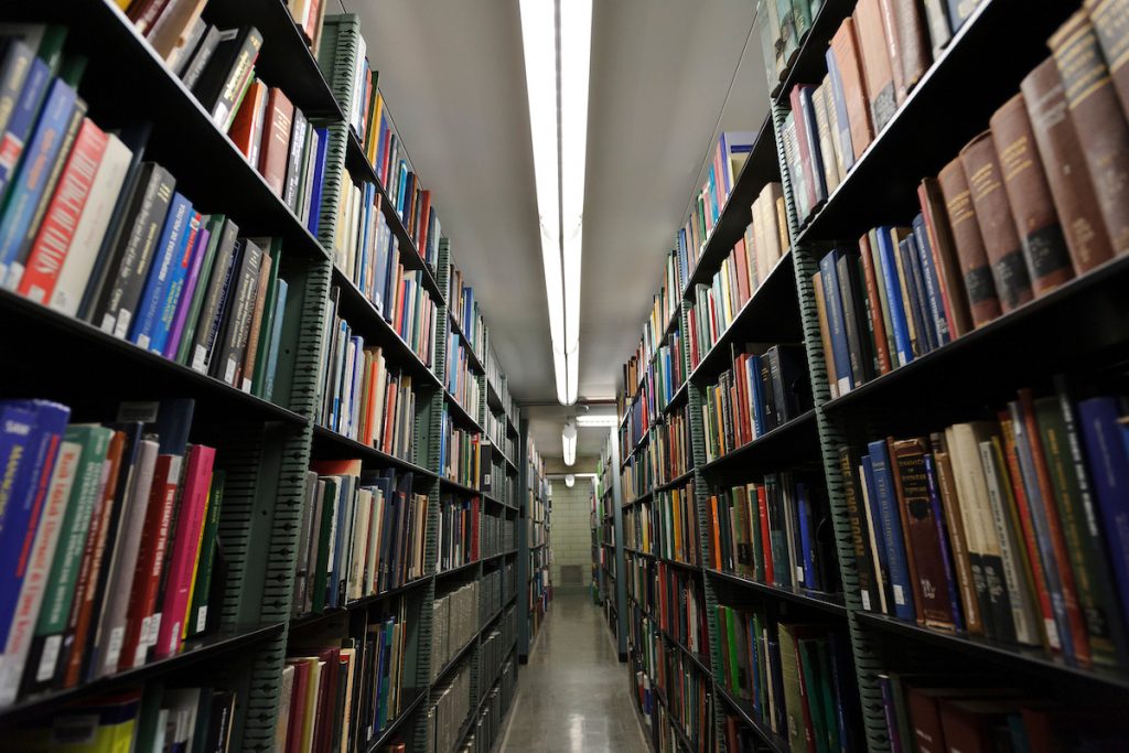 Two rows of bookshelves facing each other at Memorial Library, with a long white overhead light shining between them.